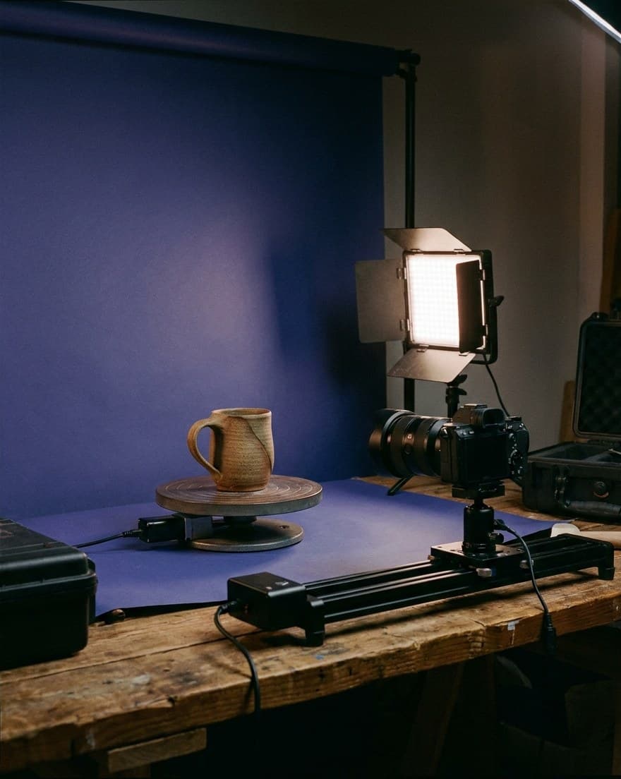 Beispielbild: Keramiktasse auf einem Drehteller vor Papierhintergrund, daneben eine LED-Leuchte und eine Kamera auf einer Schiene